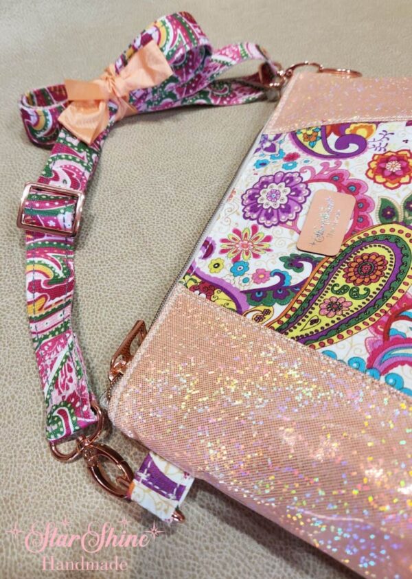 Stunning "Just Peachy" Sunshine Crossbody Crossbody. Measures 10 1/2" wise x 8" tall and 3" deep. $85.00 Colorful paisley floral fabric center, with striking holographic peach glitter vinyl. Rose gold hardware really ins striking in this combination. The exterior back also has a sipper pocket with rose gold zipper teeth and zipper pull. Matching adjustable strap in paisley and can be worn as a side strap or crossbody. Interior is waterproof canvas in rose gold color. It as a roomy slip pocket and zipper pocket.