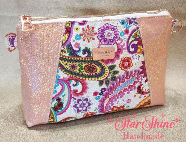 Stunning "Just Peachy" Sunshine Crossbody Crossbody. Measures 10 1/2" wise x 8" tall and 3" deep. $85.00 Colorful paisley floral fabric center, with striking holographic peach glitter vinyl. Rose gold hardware really ins striking in this combination. The exterior back also has a sipper pocket with rose gold zipper teeth and zipper pull. Matching adjustable strap in paisley and can be worn as a side strap or crossbody. Interior is waterproof canvas in rose gold color. It as a roomy slip pocket and zipper pocket.